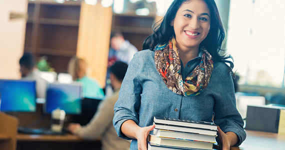 Female student in a library smiles while holding books in her hands